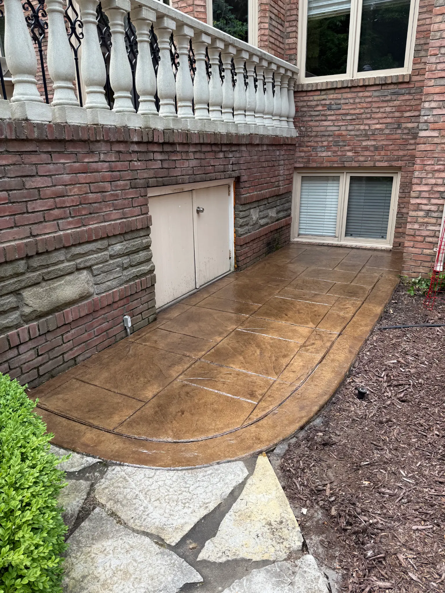 A real curved stamped concrete walk under a brick balcony, freshly sealed.